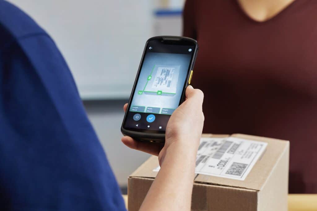 Lean logistics : en quoi cette méthode peut-elle sauver votre organisation logistique en période de fêtes ? Femme scannant un colis avec un pda Zebra en plan rapproché et écran affichant une capture photo et mesure du colis