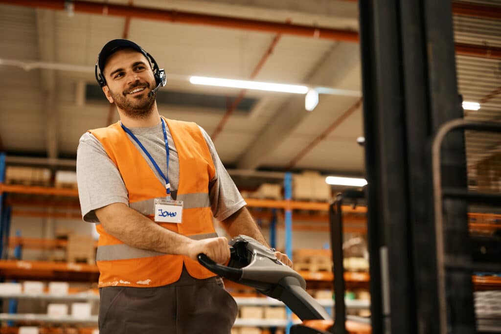 Lean logistics : en quoi cette méthode peut-elle sauver votre organisation logistique en période de fêtes ? Heureux travailleur masculin utilisant un transpalette tout en travaillant dans un entrepôt de distribution.