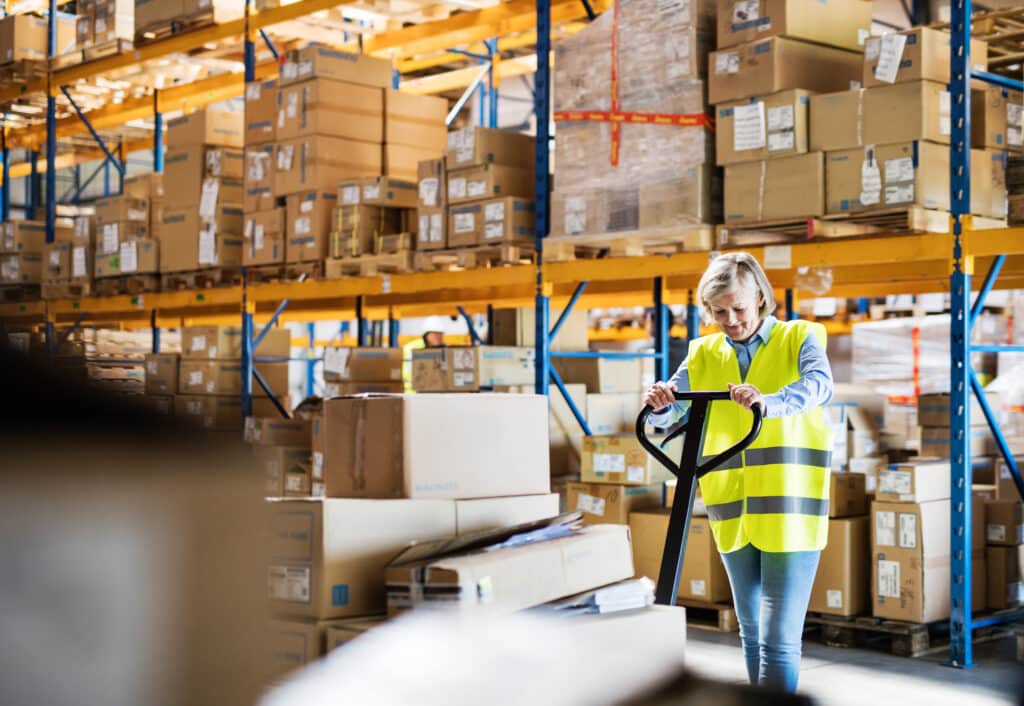 Lean logistics : en quoi cette méthode peut-elle sauver votre organisation logistique en période de fêtes ? Une employée d'entrepôt ou un superviseur senior tirant un transpalette avec des boîtes.